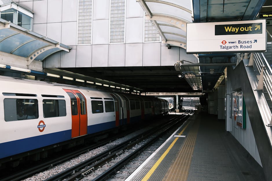 The interior of a modern London Underground train carriage with an open sliding door, revealing a single row of blue fabric-covered seats along the wall opposite the doorway. The seats have a textured
